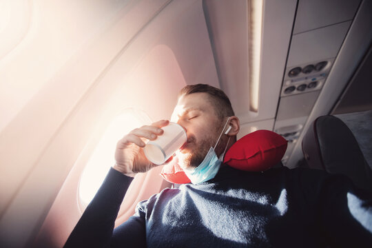 Male passenger of airplane drinks water before takeoff enjoys pillow for sleeping in chair. Concept travel with safe mask