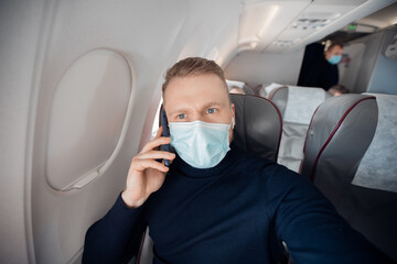 Fototapeta na wymiar Male with safe mask passenger of airplane talking on cell phone in chair. Concept travel covid