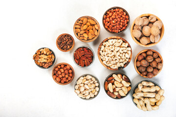 Assortment of nuts in bowls. Cashews, hazelnuts, walnuts, pistachios, pecans, pine nuts, peanuts, macadamia, almonds, brazil nuts. Food mix on white background, top view, copy space