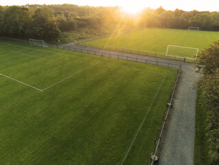 Aerial drone view on a small soccer pitch. Football training ground from above view. Sunset time. Sun flare. Empty green grass field