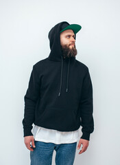 Portrait of handsome bearded hipster guy wearing black blank hoodie and baseball cap with space for your logo or design. Mockup for print. Hoodie design and advertising concept.