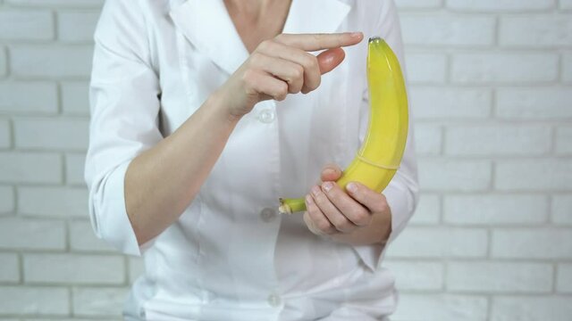 Doctor with a condom on a banana. The female doctor with a condom on a banana says.