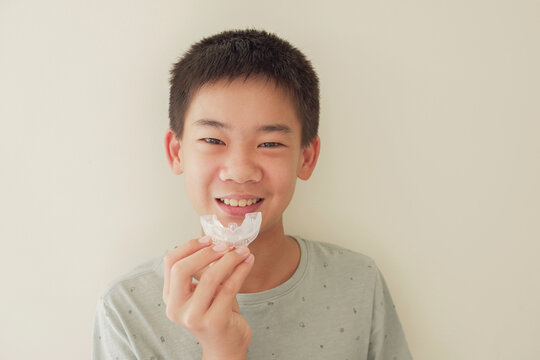 Smiling Asian preteen boy holding invisalign braces, mouthguard, teen orthodontic oral health care concept