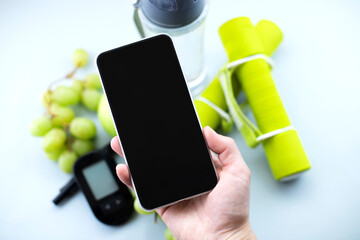 Glucose meter, lancelet, sport equipment and water with mobile phone in hand mock up. Diabetes prevention and treatment concept, image for mobile app