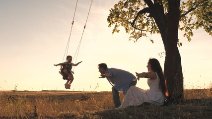 Parents swing the little girl on a swing on a summer day, flying like an airplane in the sky, happy...