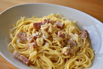 Carbonara in a white oval bowl placed on a wooden table.