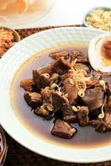 Selected Focus Rawon, Indonesian Traditional Beff Black Soup from East Java. Served on a Bowl wth Shrimp Cracker (kerupuk Udang) and Chilli Paste and Salted Egg