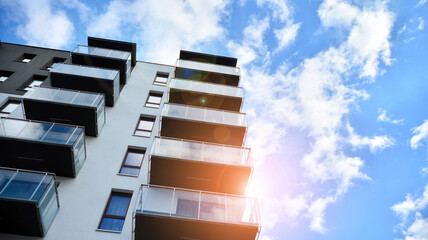 Futuristic square architecture of apartment building. Real estate with panoramic windows and blue sky with clouds.