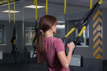 Woman in the gym doing sports with her weight on the trainer with rubber bands