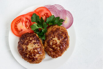 Homemade cutlets with tomatoes and purple onions on a plate, on a white background.