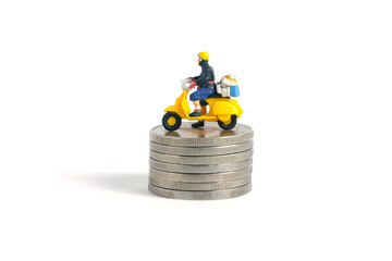 Miniature people toys conceptual photography. Cash on delivery and shipping cost service. Postman courier standing above money coin stack, isolated white background.