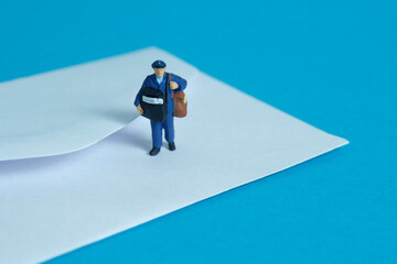 Miniature people toys conceptual photography. Mail postal courier delivery. Postman courier with envelope, isolated on blue background.