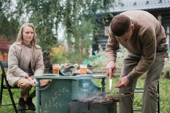 A Young Eastern European Man Prepares A Barbecue, Roasts Fragrant Meat On The Grill. Concept Of A Romantic Picnic For A Young Couple