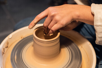 beautiful hands of a young girl, stained with clay when modeling a pot on a potter's wheel in the workshop