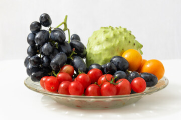 Multiple fruit combination platter isolated on white background, cherry tomatoes, black grapes, cherimoya and kumquat