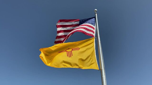 Flags of United States of America and the State of New Mexico waving in the wind against a blue sky