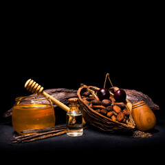 Cocoa pod and cocoa beans with cherry, bourbon vanilla, tobacco pipe, glass jar of honey and bottle of oil on a black background. Copy space.