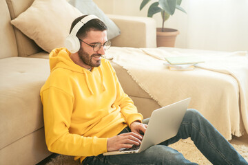 Smiling man student in wireless headphone and glasses study online with laptop at home. Distance learning and online teaching concept.
