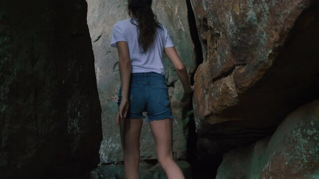 A young woman steps through between a large colorful rock and a rocky mountain cliff in Tennessee, exploring nature and discovering new views, reconnecting and achieving goals, slow motion