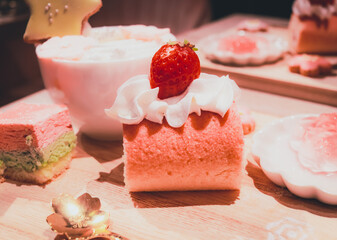 Sakura Roll Cake with a strawberry on top on a cake plate with a cup in the background