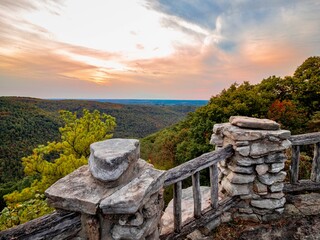 Overlook of the mountains and the fall foliage at Coopers Rock State Forest in West Virginia with the sunset golden sky one direction and a blue swirly sky the other direction, with the rock cliff.