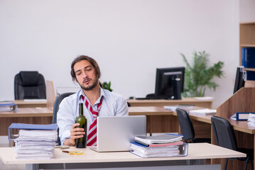 Young male employee drinking alcohol in the office