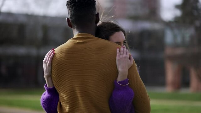 Interracial couple embrace outside. Young woman hugs partner