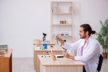 Young male chemist sitting at the desk in the classroom