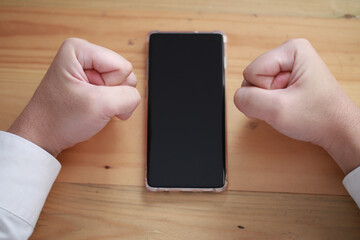 Angry man clasp his fist on table with smart phone, mobile phone mock up