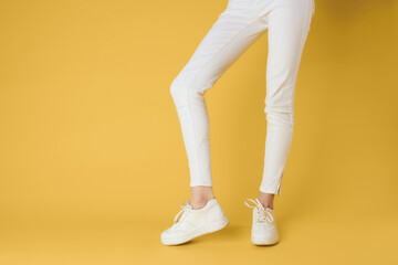 Fototapeta na wymiar Womens legs white pants sneakers fashion clothes luxury street style yellow background