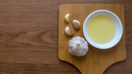 Selective focus of garlic and its oil on wooden background with copy space.