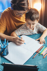 Upper view photo of a careful mother helping her son doing the homework writing something in the copybook