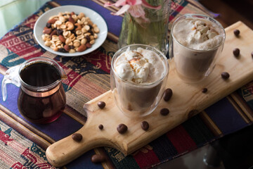 Affogato-style coffee on a glass table and tablecloth accompanied by black coffee and assorted beans, including peanuts, raisins and almonds.