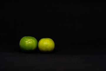 Two lemons have both green and yellow with black background.