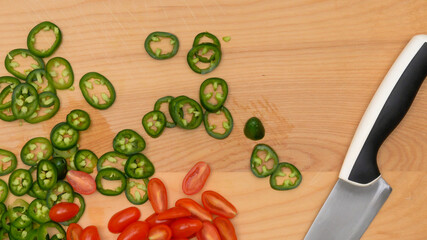 Green chili pepper and cherry tomato slices close up on rustic wooden background, close up view directly from above