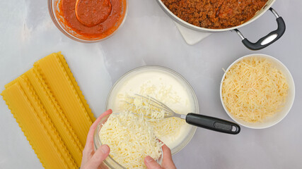 Mix of cream cheese, milk, and mozzarella cheese in a glass bowl close up in woman hands. Step by step beef lasagna recipe