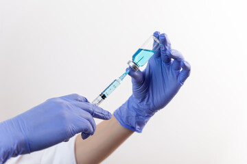 Woman hands in purple rubber gloves holds and fills syringe from bottle with blue vaccine