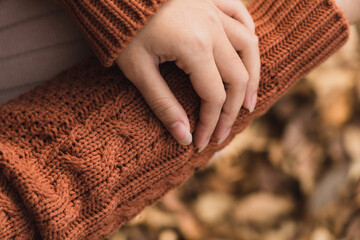 Woman wearing orange knitted sweater hand posing with autumn falling leaves