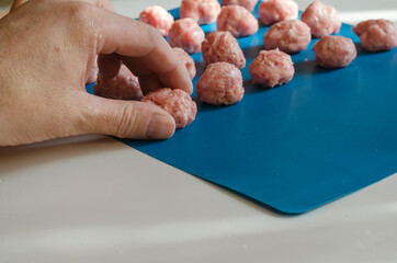 Male hand puts meatballs on a blue surface.