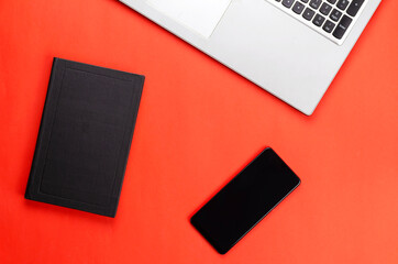 Hardcover book, phone, laptop on a red background.