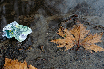 A crumpled ˆ 100 bill lies on the wet ground.