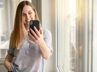 Pretty young woman with mobile phone by the window