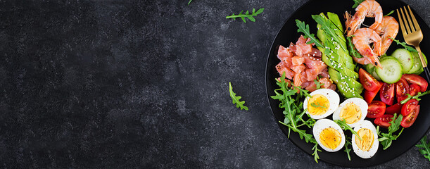Fototapeta na wymiar Ketogenic diet breakfast. Salt salmon salad with boiled shrimps, prawns, tomatoes, cucumbers, arugula, eggs and avocado. Keto, paleo lunch. Top view, banner