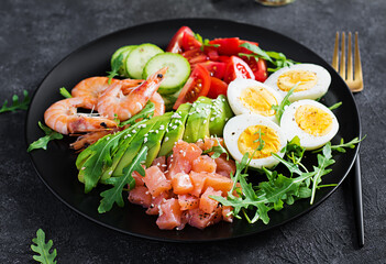 Ketogenic diet breakfast. Salt salmon salad with boiled shrimps, prawns, tomatoes, cucumbers, arugula, eggs and avocado. Keto, paleo lunch.