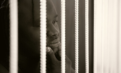 Jailed african american black man rubbing his chin behind bars. High quality photo