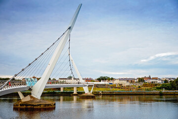 Derry, Ireland. Illuminated Peace bridge in Derry Londonderry, City of Culture, in Northern Ireland with city center at the background. Night cloudy sky with reflection in the river at the dusk