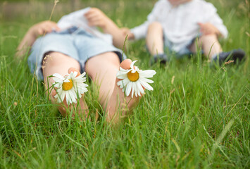 Kid having fun at spring nature. Child feet with daisy flower. Boy lying on green grass outdoors in park. Happy summer feet. Child with daisy lying in sunny meadow and relaxing in summer sunshine.