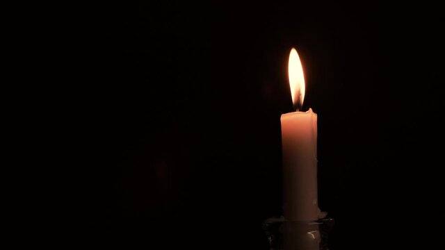 Close-up burning single candle flame isolated on black background, 4K video