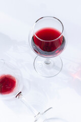 A glass of red wine on the white table with leaves shadows modern composition. Close up	