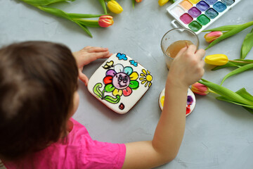 a girl paints a gingerbread with food dyes. A coloring book for children lies on a gray table. the concept of an original edible gift for a child.